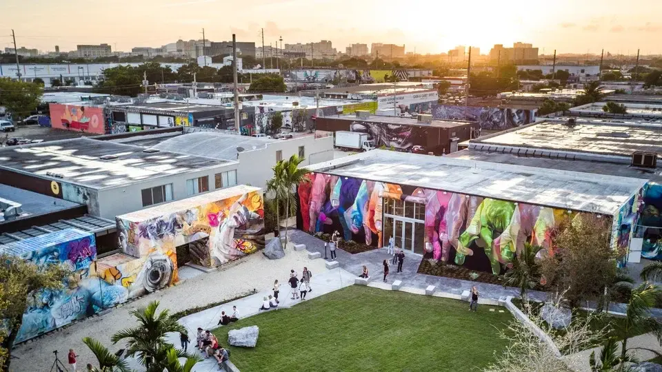 Praça com gramado grande, muros com graffiti e um por do sol ao fundo