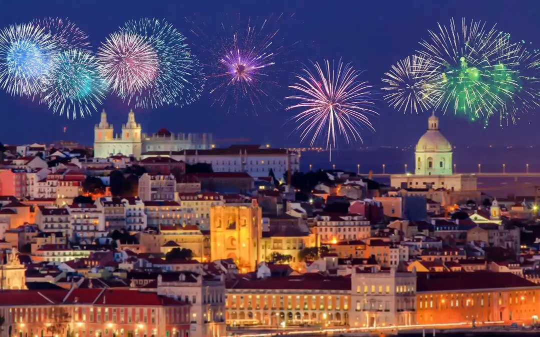 Fogos de artifício coloridos iluminam o céu sobre os edifícios históricos de Lisboa durante as celebrações de Ano Novo.