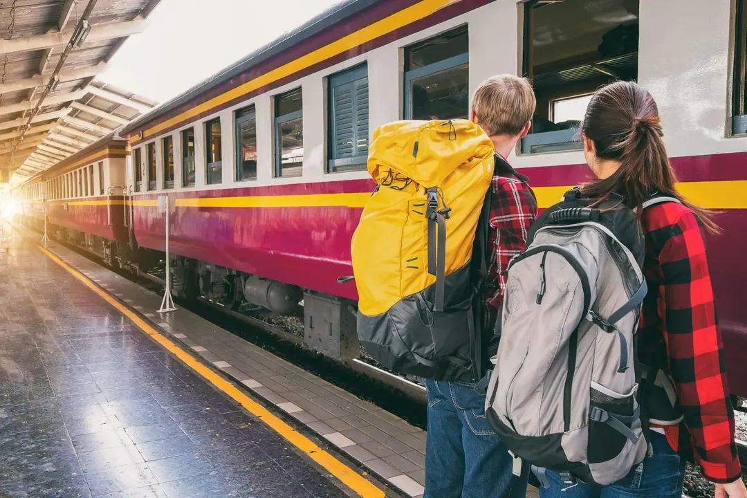 Casal de jovens com mochilas esperando um trem para embarcar,