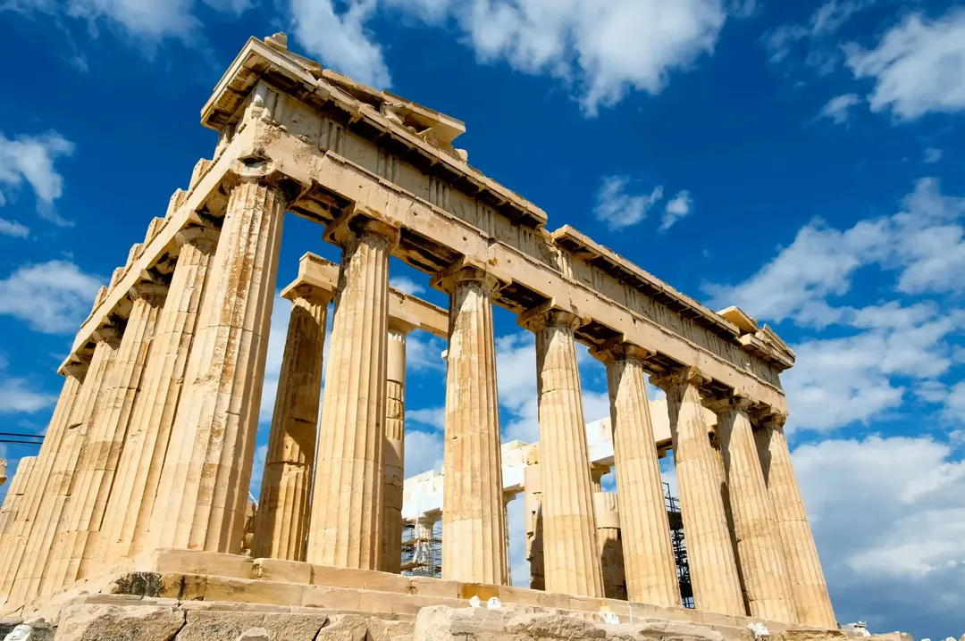 Vista do Partenon em Atenas, Grécia, com suas colunas de mármore dourado sob um céu azul com nuvens esparsas.