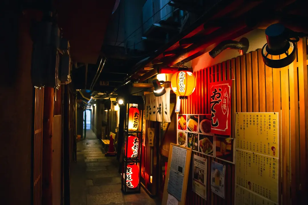 Rua estreita em Kyoto, Japão, à noite, com letreiros de restaurantes e lanternas japonesas iluminadas.
