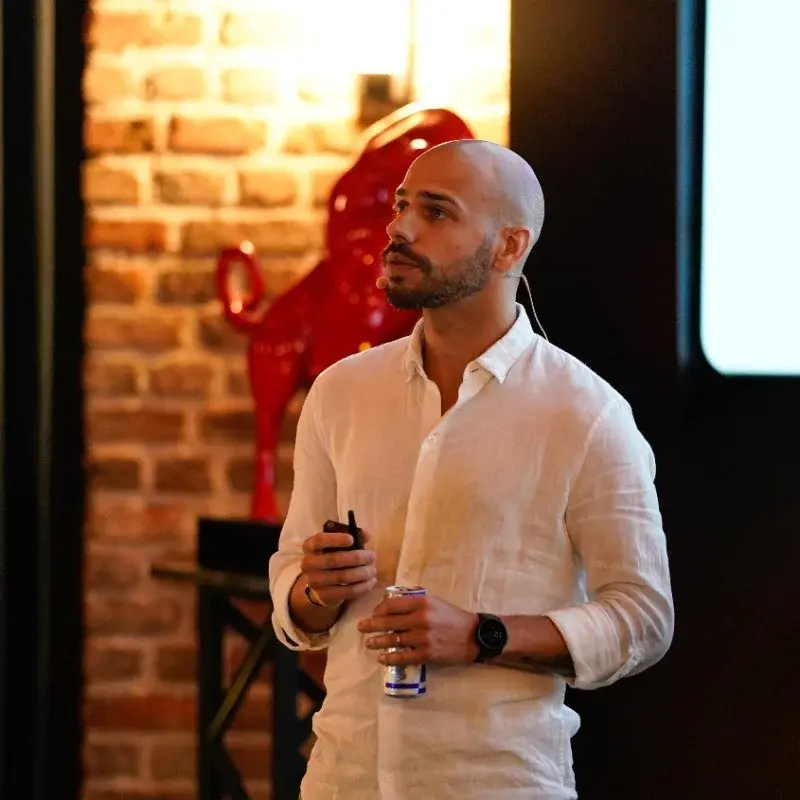 homem careca de camisa branca, segurando uma lata de redbull e um controle