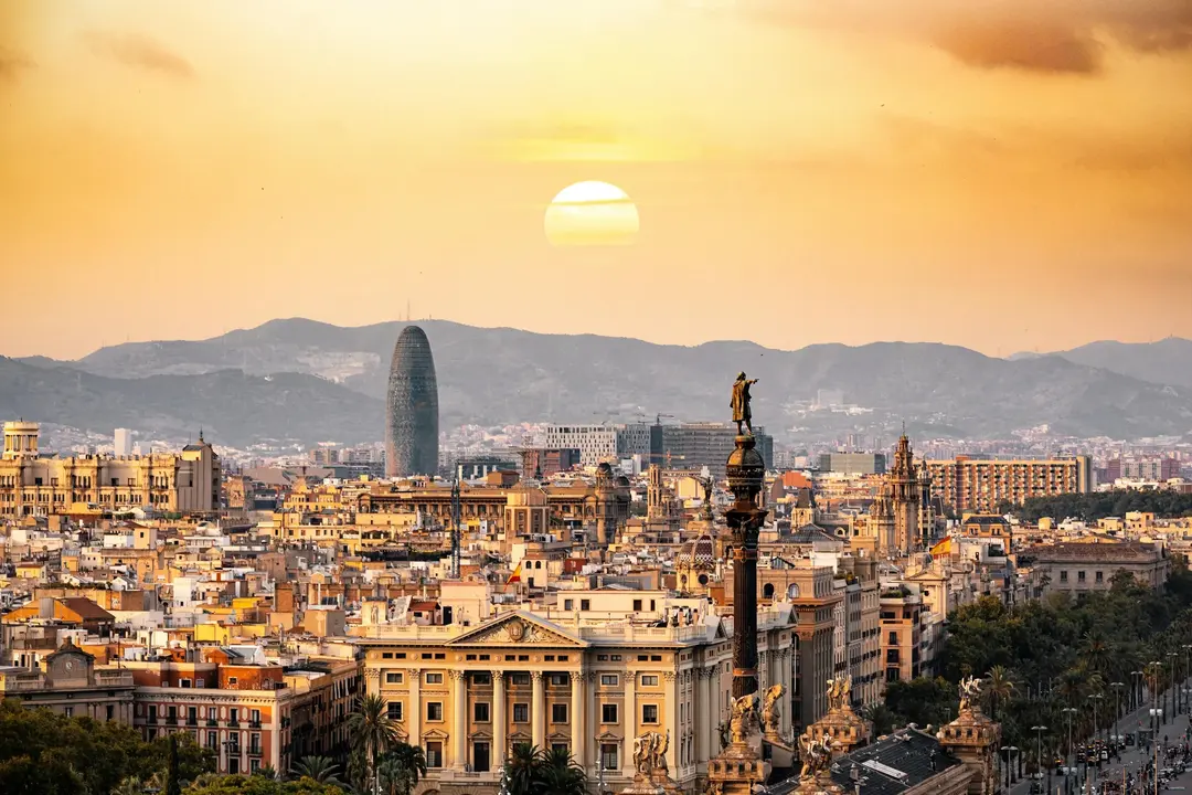 Vista de Barcelona ao pôr do sol com a estátua de Colombo e a Torre Agbar, um destino na Europa cheio de cultura e história.