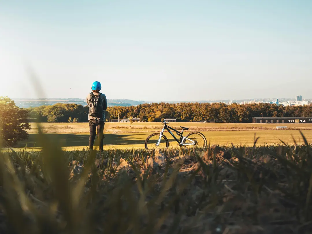 Homem olhando para campo ao lado de uma bicicleta.