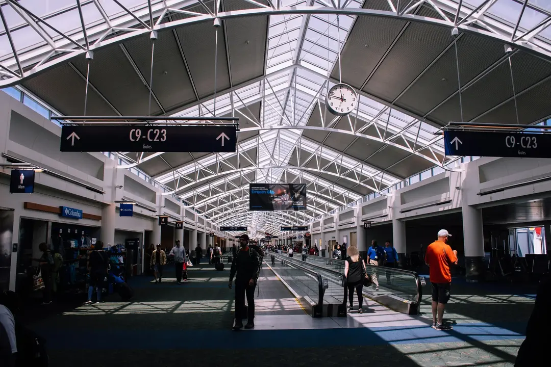 Interior de um aeroporto movimentado, com pessoas caminhando e placas indicando os portões de embarque.