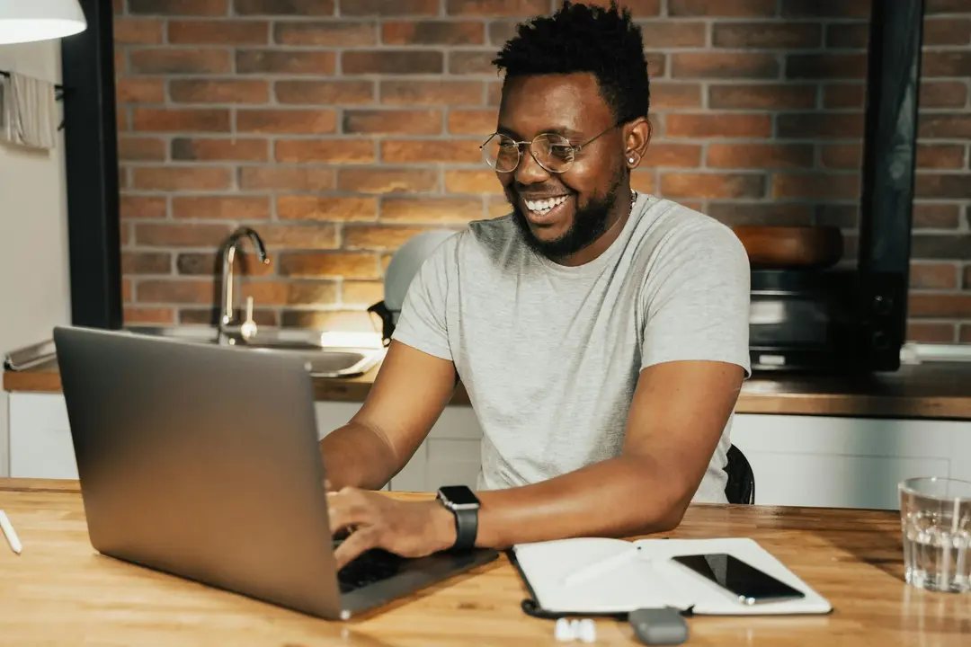 Homem feliz trabalhando em casa com seu laptop, conferindo as melhores dicas para economizar em passagens.