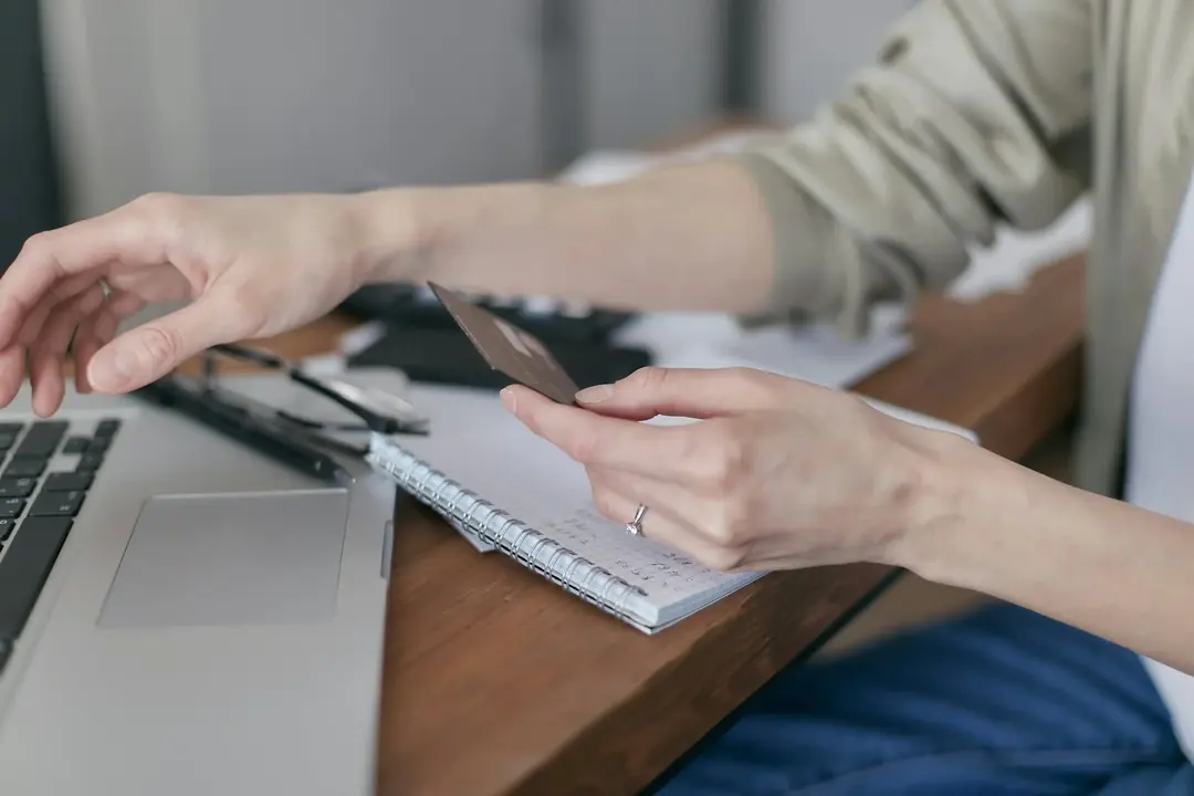 Pessoa segurando um cartão de crédito, pronta para garantir as melhores tarifas de voo no laptop.